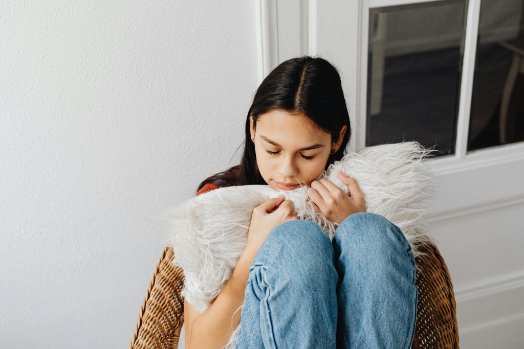 A woman sitting on a chair and hugging a pillow.