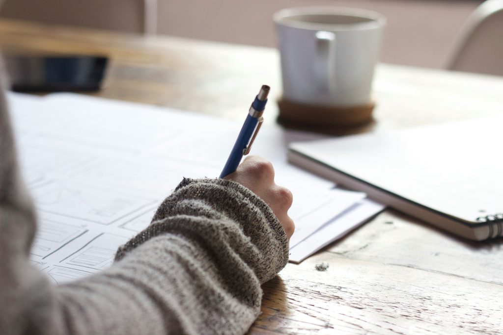 Person writing on paper with a mug in the background